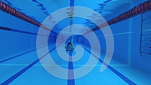 sportswoman swimmer in a tracksuit, in diving goggles, in a swimming cap is training in the pool. The athlete swims