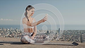 Sportswoman taking selfie on smartphone at city. Yoga woman sitting in lotus pose