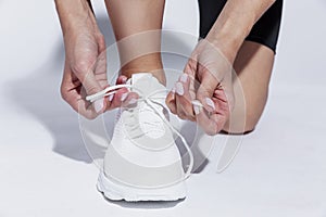 The sportswoman is tying the laces on the shoes. Close-up. Hard sunlight, white background