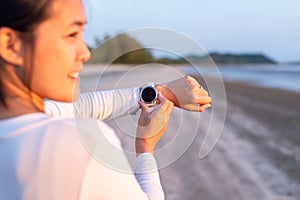 Sportswoman using smart watch for running and checking device at the beach during sunset