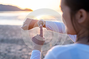 Sportswoman using smart watch for running and checking device at the beach during sunset