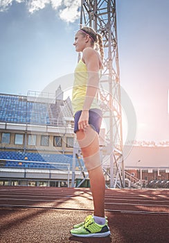 Sportswoman wearing t-shirt and shorts standing on a red running track in athletics stadium.