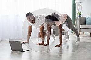 Sporty african american couple having online fitness class, using laptop