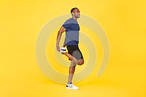 Sporty African American Male Exercising Stretching Leg Over Yellow Background