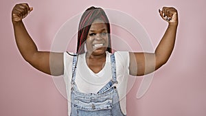 Sporty african american woman confidently flashing a strong arm gesture, smiling over a pink isolated background, emanating joy