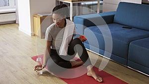 Sporty african american woman drinking water after workout at home on yoga mat