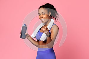 Sporty African American woman holds water bottle pointing finger, studio