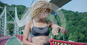 sporty african american woman looking at her sport bracelet on hand checking data on fitness tracker after jogging