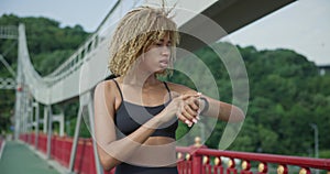 sporty african american woman looking at her sport bracelet on hand checking data on fitness tracker after jogging