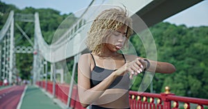 sporty african american woman looking at her sport bracelet on hand checking data on fitness tracker after jogging