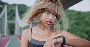 sporty african american woman looking at her sport bracelet on hand checking data on fitness tracker after jogging