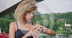 sporty african american woman looking at her sport bracelet on hand checking data on fitness tracker after jogging