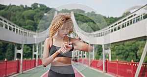 sporty african american woman looking at her sport bracelet on hand checking data on fitness tracker after jogging