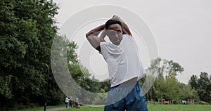 Sporty african man with warm up by stretching arms before running in city park. Sportsman doing workout outdoors