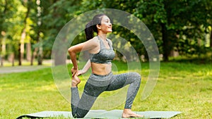 Sporty Asian girl doing yoga stretching exercises on mat at summer park