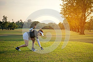 Sporty asian golfer woman putting golf ball on tee with club in golf course on sunny day for healthy sport.