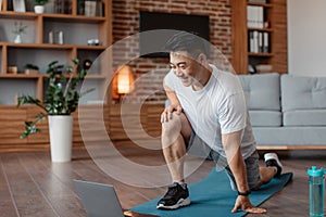 Sporty asian mature man exercising at home, warming up before training and using laptop, training at home