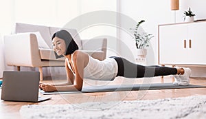 Sporty asian woman doing plank watching tutorial on laptop