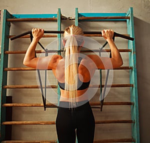 Sporty athlete woman exercising doing pull-ups in gym from back