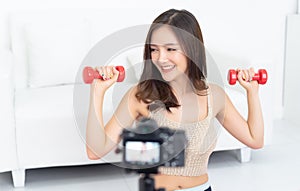 Sporty beautiful Asian woman blogger recording a video exercising at home to stay fit.