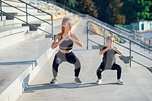 Sporty beautiful elder and younger sisters which squating together during fitness training outdoors.