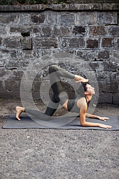 Sporty beautiful young woman practicing yoga working out, wearing sportswear, outdoor full length, brick wall background