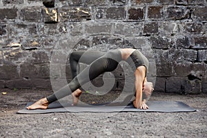 Sporty beautiful young woman practicing yoga working out, wearing sportswear, outdoor full length, brick wall background