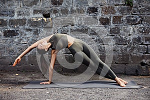 Sporty beautiful young woman practicing yoga working out, wearing sportswear, outdoor full length, brick wall background