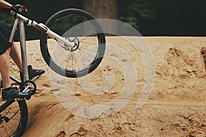 A sporty bicycle rider takes off powerfully while mountain biking at a dirt jumpline in the woods.