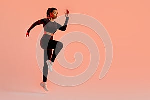 Sporty black lady jumping, having cardio training, wearing black fitwear, exercising over neon background, free space