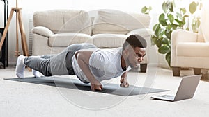 Sporty Black Man Making Fist Plank Exercise In Front Of Laptop