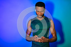 Sporty Black Man Using Phone And Earphones On Blue Background