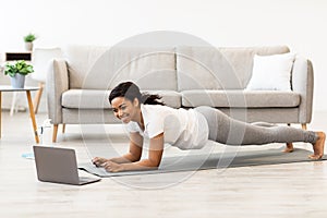 Sporty black woman doing plank watching tutorial on laptop