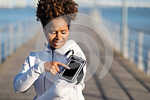 Sporty Black Woman Touching Smartphone Screen In Armband Before Running Outdoors