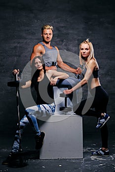 Sporty blond and brunette women and an athletic man over grey ba