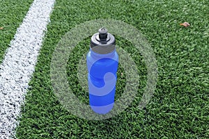 Sporty blue water bottle on the background of a green football field with a white sideline.