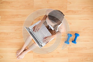 Sporty brunette using a laptop and sitting next to dumbbells