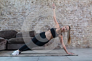 Sporty Caucasian girl doing side plank star exercise working abs and oblique muscles indoors against brick wall