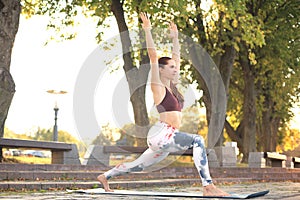 Sporty concentrated woman practicing yoga, standing in anjaneyasana pose, working out in park on sunset