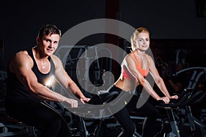 Sporty couple exercising at the fitness the exercise bike on a dark gym.