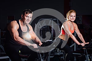 Sporty couple exercising at the fitness the exercise bike on a dark gym.