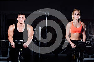 Sporty couple exercising at the fitness the exercise bike on a dark gym.