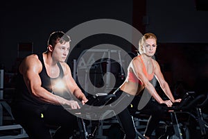 Sporty couple exercising at the fitness the exercise bike on a dark gym.