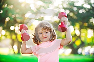 Sporty cute blonde boy with dumbbells outdoor. Fitness kids, health and energy. Healthy kids lifestyle. Kid exercising