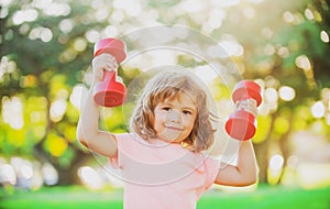 Sporty cute blonde boy with dumbbells outdoor. Fitness kids, health and energy. Healthy kids lifestyle. Kid exercising