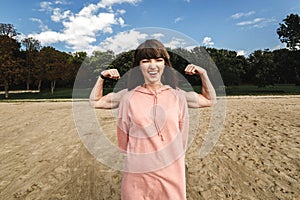 Sporty energetic athletic woman wears pink sports top smiles as shows her biceps, likes sport and active lifestyle