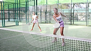 Sporty European woman playing padel tennis during a friendly doubles match on an outdoor court.