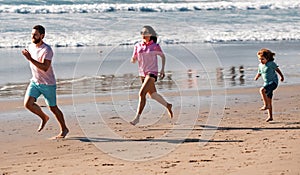 Sporty family father, mother and baby son jogging, child run by water pool along sea surf on black sand beach. Travel