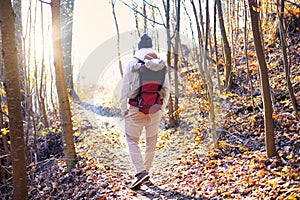 Sporty father carrying his infant son wearing winter jumpsuit and cap in backpack carrier hiking in autumn forest.