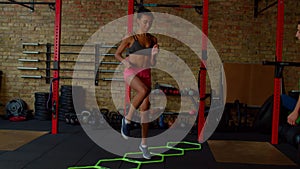 Sporty fit black woman practicing high knee walking exercise with agility ladder